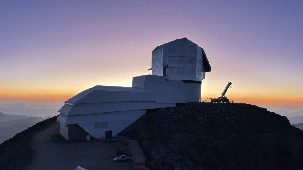 Astronomical observatory situated on a rocky hillside during sunset, with a gradient sky transitioning from orange to purple.